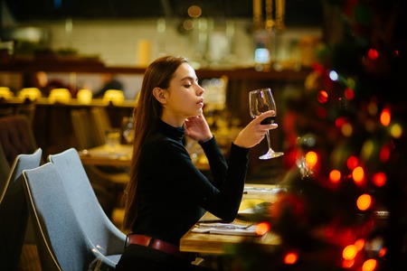 Winter holidays celebration concept. Girl with long hair celebrate new year and christmas. Festive fashion, style, decorations. Xmas party drinks, toast, alcohol. Woman enjoy wine in restaurant.の写真素材