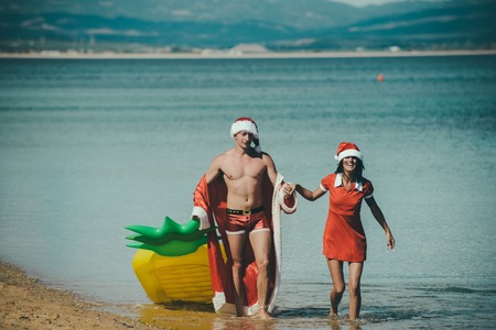 Xmas party celebration and activity. Christmas couple with pineapple inflatable mattress. New year girl and guy as santa. Couple in love of happy man and woman in water. Winter holiday and vacation.の写真素材