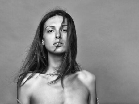 Pretty brunette woman or girl with long hair which falling on her neck touching lips on gray studio background, copy spaceの写真素材