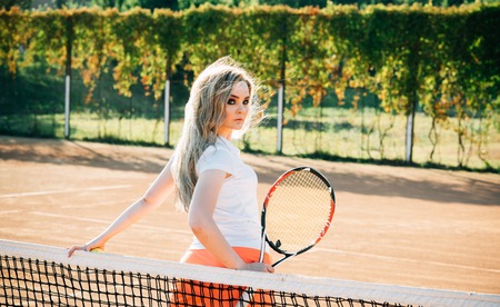 Activity, energy, health. Woman player with tennis racket on sunny day. Sport, game concept. Girl athlete in tennis uniform at net on court. Tennis fashion, clothing, wear.の写真素材