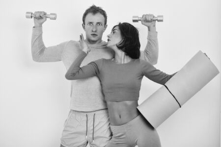 couple of pretty woman or cute girl with fitness mat and handsome surprised guy man with muscular torso and sexy body training in sport gym with dumbbells isolated on white backgroundの写真素材