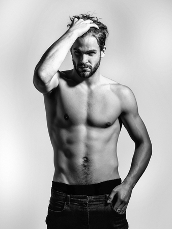 Handsome guy fashion sexy young bearded macho man model in pants with bare muscular torso and chest on grey backgroundの写真素材
