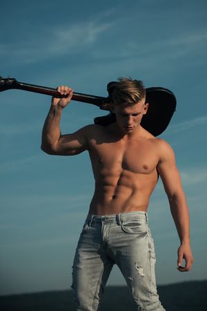 Athlete guitarist with six pack, ab outdoor. Man with muscular torso hold electric guitar on blue sky. Sport, fitness, health concept. Music, performance, entertainment. Training and playing.の写真素材