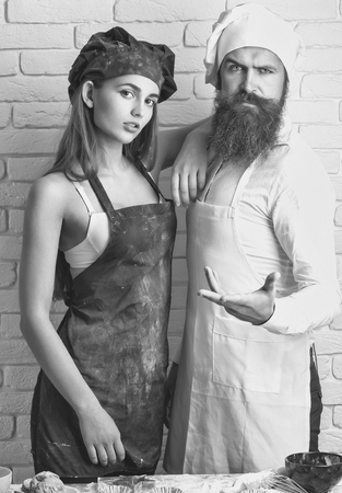 Bearded man, handsome cook or baker and pretty girl or beautiful woman in red apron messy with flour and whisk in bowl on white kitchen wallの写真素材