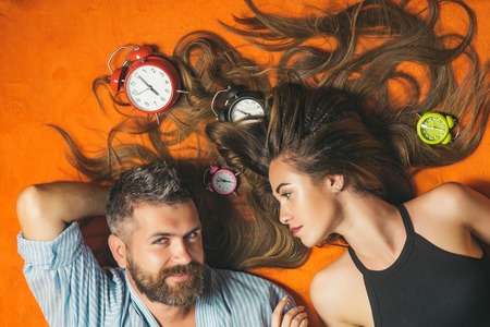 Bearded man and woman with long hair, time. Couple in love sleep on floor with alarm clock. Relations, relax, wake up. Love and romance, perfect morning. Happy family laying tired with clock, trust.の写真素材