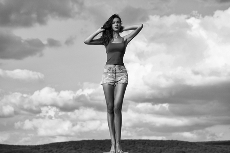 pretty girl or woman young slim fashion model in ripped denim shorts poses outdoors over blue cloudy sky natural backgroundの写真素材