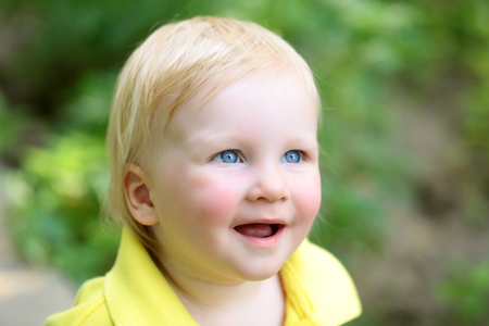Boy infant smile with blue eyes on adorable face and blond hair on natural environment. Child,...