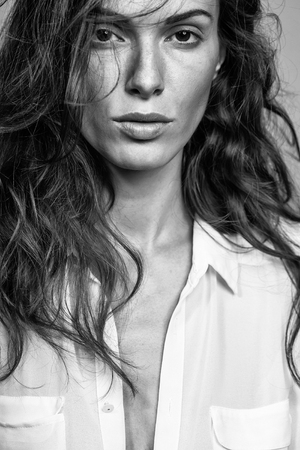 young sexy woman with pretty face and long brunette curly hair in white shirt has slim body in studio on grey backgroundの写真素材