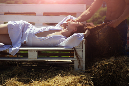 Girl with long hair and male torso with muscle. Woman relax on bench on sunny summer day. Romance, relationship, family. Beauty, look concept. Vacation, travel, wanderlust.の写真素材