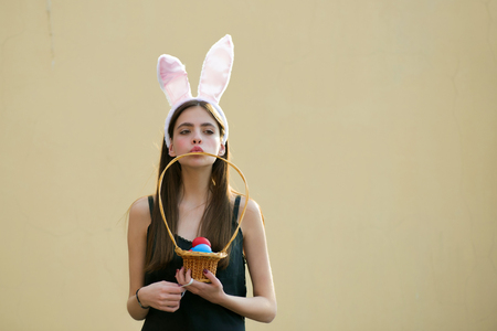 Easter girl with rosy bunny ears on beige background. Woman holding wicker basket with colored eggs. Fertility and rebirth concept. Easter tradition and symbol. Spring holiday celebration, copy spaceの写真素材
