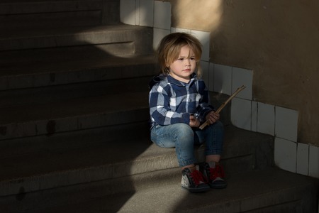 Boy with blond hair sit on house stairs. Toddler in blue shirt, jeans, shoes hold stick on staircase. Future, success concept. Child, childhood, lifestyle. Kid fashion, style.の写真素材