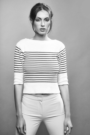 young stylish woman or girl with glamour makeup on pretty face in striped fashionable cloth on slim sexy body posing in studio on grey backgroudの写真素材