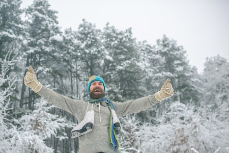 Man in thermal jacket, beard warm in winter. Temperature, freezing, cold snap, snowfall. Winter sport and rest, Christmas. Bearded man with skates in snowy forest. skincare and beard care in winter.の写真素材
