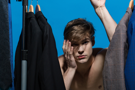 Macho with unhappy face choose clothes in wardrobe on blue background. Fashion, style concept....