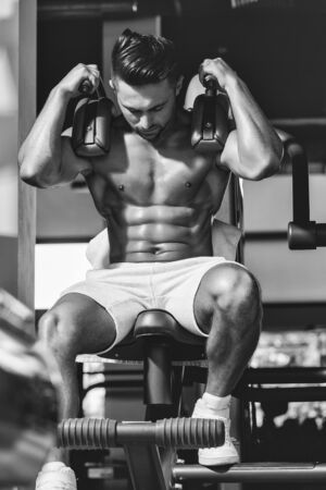 Handsome young man with sexy muscular wet body and bare back training with heavy exercise equipment in gymの写真素材
