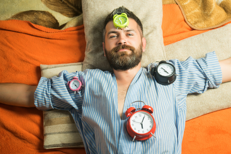 Time management, perfect morning. Relax and wake up, time. Tired hipster with clock. Man with clock in bedroom, loneliness. Bearded man sleep on floor with alarm clock.の写真素材