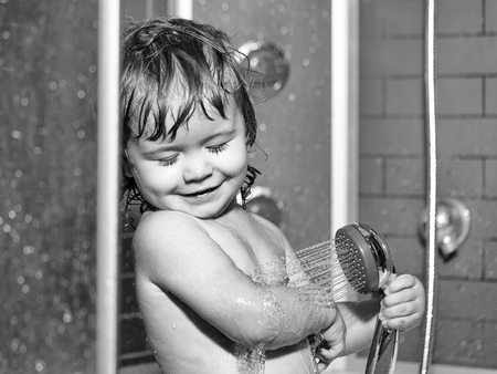 Cute happy smiling funny undressed boy child with blonde curly wet hair taking shower in bath with water indoor, horizontal pictureの写真素材