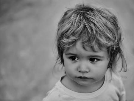Cute baby boy child with brown eyes and curly blond hair in yellow shirt outdoors on beige backgroundの写真素材