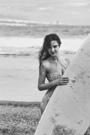 Pretty happy girl, surfer, or beautiful woman, sexy slim brunette, in sexi swimsuit with yellow surfboard on sandy beach outdoors on sunny summer day on blue sea backgroundの写真素材