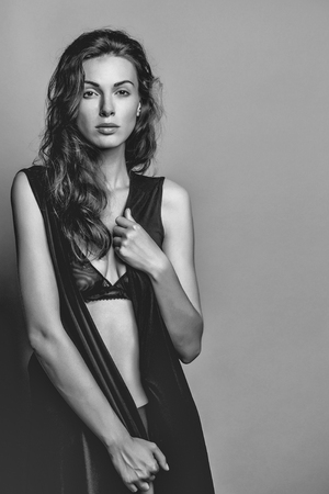 young sexy woman with pretty face and long brunette curly hair in black bra and panties has slim body in studio on grey backgroundの写真素材