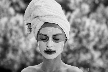 Pretty cute woman or girl with facial mask and white towel on head on sunny natural green background