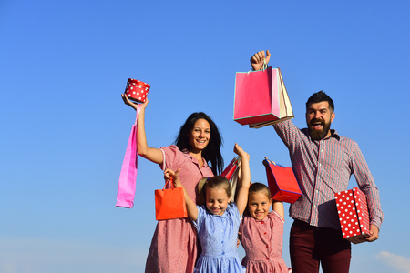 Man, woman and adorable children with gifts on sky background. Mother, father and kids with bags and packs. Family with smiling faces open presents outside. Happy family and shopping concept.の写真素材