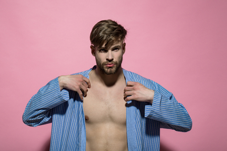 Man put blue dressing gown on pink background. Macho with sexy torso in bathrobe. Home clothes, leisure wear. Spa, wellness, grooming. Fashion, style concept.の写真素材