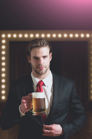 beer glass in hand of man or businessman with beard and hairstyle in formal outfit with red tie near mirror with lamps, meeting and relax, bar and restaurant, sommelier, tasting and degustationの写真素材