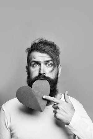 young bearded man with romantic face holding red paper heart in studio on grey background, copy spaceの写真素材