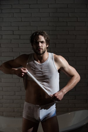 Spa and relaxation, sexy man. Hygiene and healthcare. Man with muscular body in bath. Bathroom and home comfort. Guy with wet hair sitting in bath tub.の写真素材