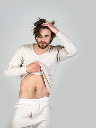 Sleepy man with beard on grey background. Man with disheveled hair in underwear. Morning wake up, everyday life. Insomnia, energy, single with uncombed hair. Barber and hairdresser, male fashion.の写真素材
