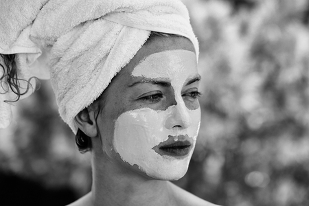 Pretty cute woman or girl with facial mask and white towel on head on sunny natural green backgroundの写真素材