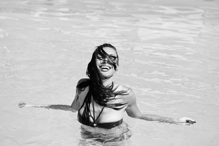 young sexy woman or girl with pretty smiling happy face and wet hair swimming in pool with blue water sunny summer day outdoorの写真素材