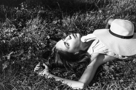 Pretty cute girl young beautiful sexy woman laying on green grass with long hair sunny summer day on natural background with hatの写真素材