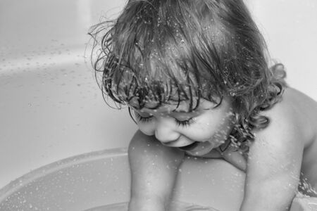 Small cute funny baby boy with blonde wet hair in bath waterの写真素材