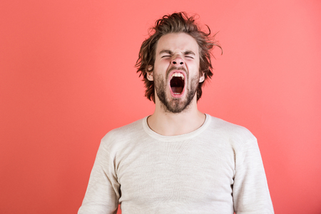 Sleepy man with beard on red background. Insomnia, energy, single with uncombed hair. Morning wake up, everyday life. Barber and hairdresser, male fashion. Man with disheveled hair yawn in underwear.の写真素材