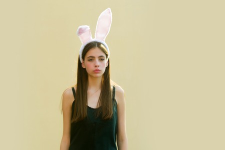 Easter girl posing on beige background. Woman wearing rosy bunny ears. Fashion model with long brunette hair and black dress. Easter holiday celebration concept, copy spaceの写真素材