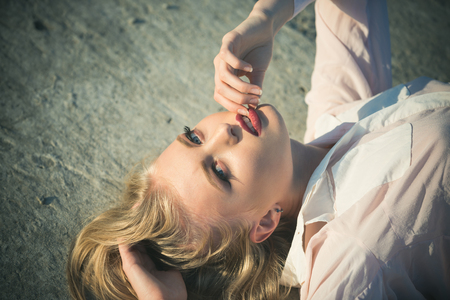 Skincare, skin, make up. Girl with long blond healthy hair lie on concrete surface. Beauty, look concept. Sensual woman with red sexy lips on makeup face outdoor. Haircare, health, hairstyle.の写真素材