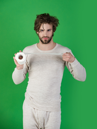 Man with serious face hold toilet paper, single. Hygiene and sanitary. WC and restroom. Sterility and purity. Man in underwear with disheveled hair, morning. diarrheaの写真素材
