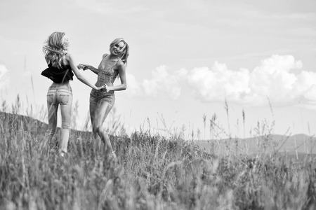 young pretty women with long lush curly blonde hair and sexy bodies standing in green field with grass and blue cloudy sky outdoor on natural backgroundの写真素材