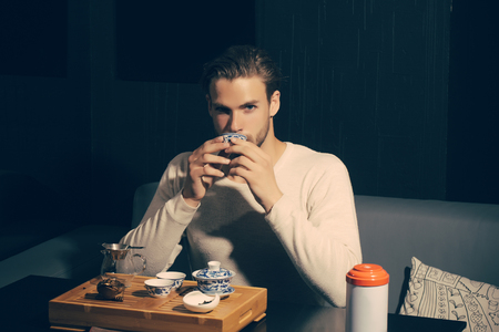 Brew tea concept. Man drink tea on sofa in cafe. Relaxation, lounge, relax. Tea party, ceremony, time. Beverage, food, cuisine.の写真素材