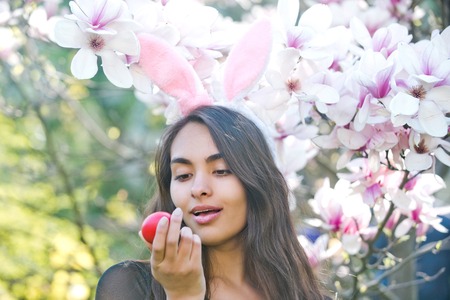 egg in hand of happy woman or adorable girl with sexy, plush lips and rosy bunny ears on long,...