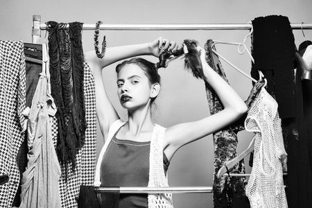 Pretty girl young sexy beautiful woman cute fashion female model with stylish hair and purple lips among clothes on hangers in wardrobe or shop on grey wall backgroundの写真素材