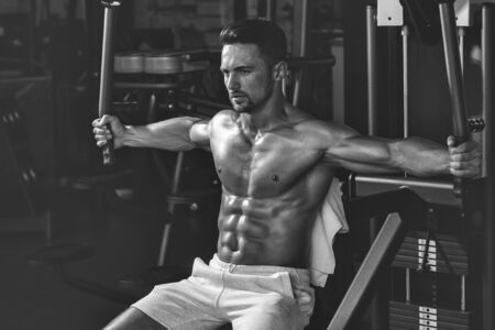 Handsome young man with sexy muscular wet body and bare back training with heavy exercise equipment...