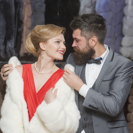 Couple in love tries expensive mink overcoats on. Rich fashion concept. Guy with beard and woman buy furry coat.の写真素材