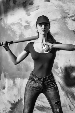 Pretty girl or sexy baseball player with blond hair in red cap, tshirt and blue jeans standing with green bat and ball on abstract yellow and pink wallの写真素材