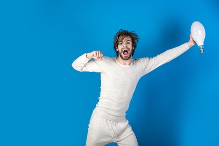happy man with disheveled hair hold big lamp as idea symbol in morning on blue background, Energy and electricity, Power and business success, solutionの写真素材