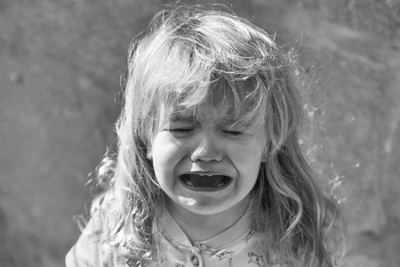 Cute unhappy baby boy with long blond hair in blue tshirt crying outdoors on sunny summer day on...