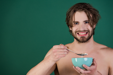 Dieting and fitness, calorie. Man with wet hair eat breakfast on green background. Food and beauty, health. Sexy man with muscular body eating cereal, healthcare. Morning, vegetarian, organic food.の写真素材