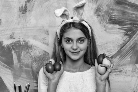 happy easter girl painter in pink bunny ears with colorful painted eggs and pencil set, has long blonde hair on abstract background. traditional spring holiday celebrationの写真素材